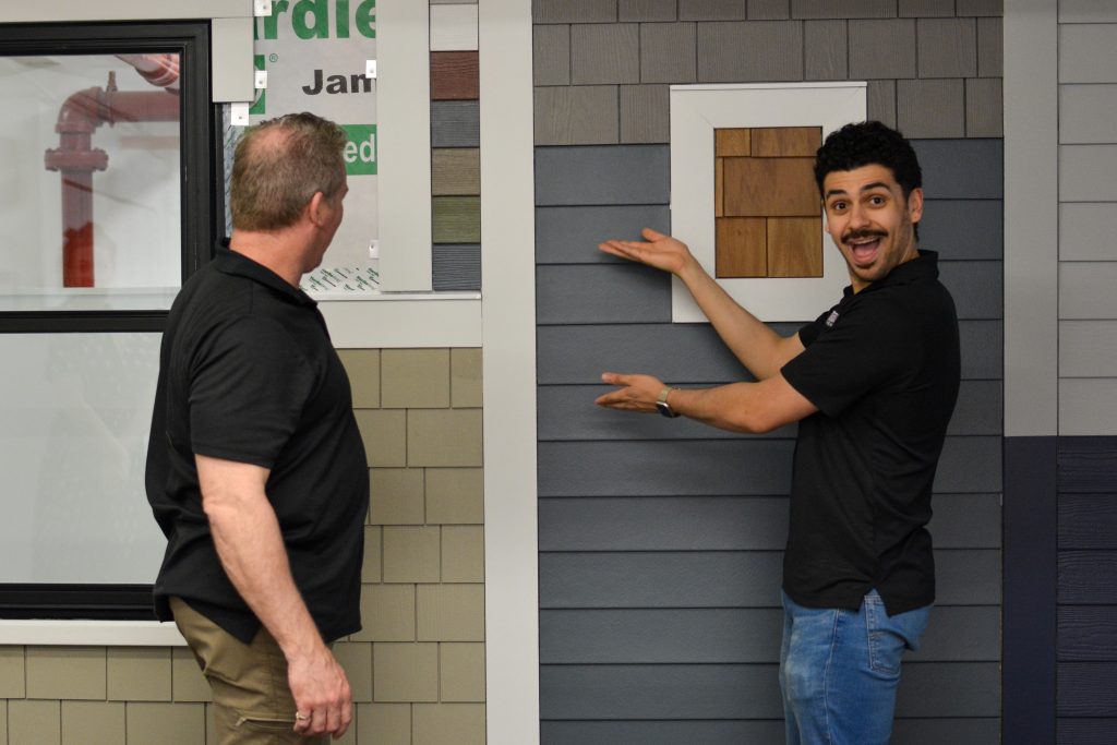 Patriot Contracting staff enthusiastically gesturing to a James Hardie siding sample wall.