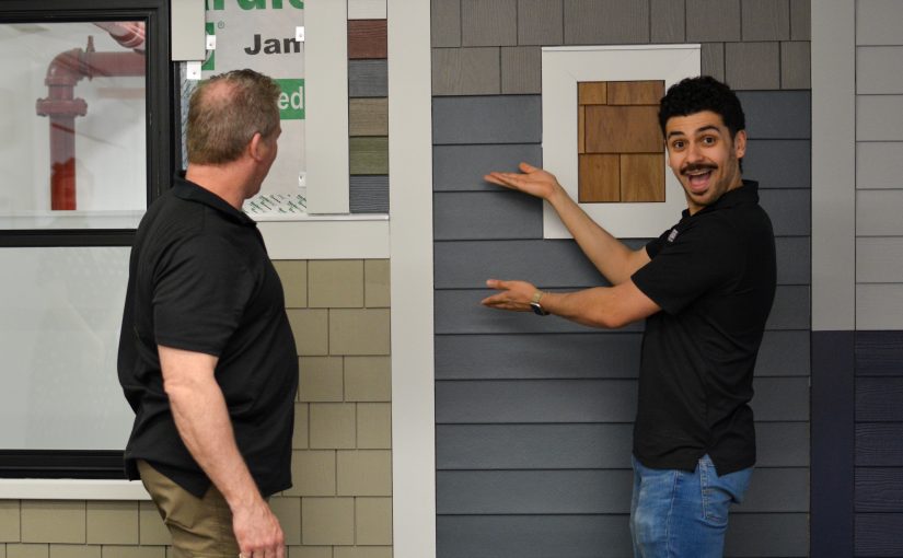 Patriot Contracting staff enthusiastically gesturing to a James Hardie siding sample wall.