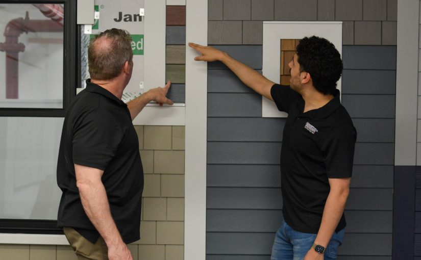 Patriot Contracting staff gesture to example siding wall.