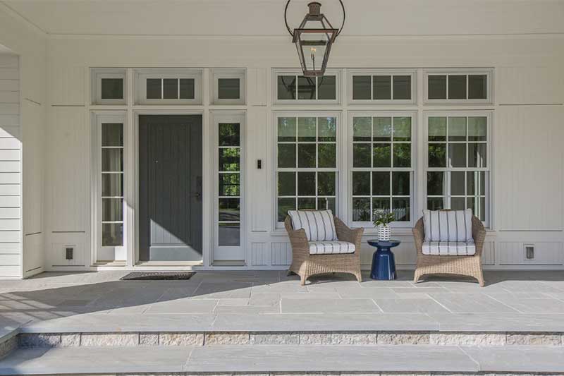 An open hardscape porch with door and windows with outdoor furniture.