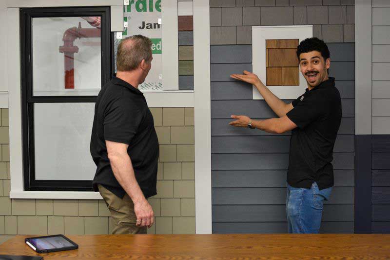 Patriot Contracting staff enthusiastically gesturing to a James Hardie siding sample wall.