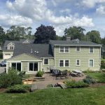 Photo of a large home with roofing, siding, and patio, with construction materials.