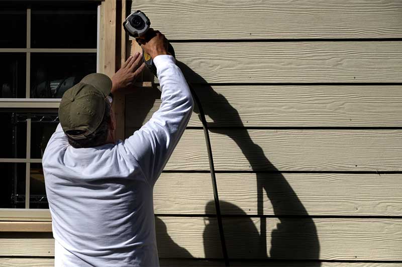 Patriot Contracting staff using a pneumatic nail gun to install siding on a home.