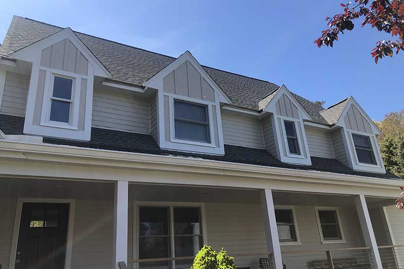 Angled shot of a house's windows, porch, and roofing beneath a blue sky.