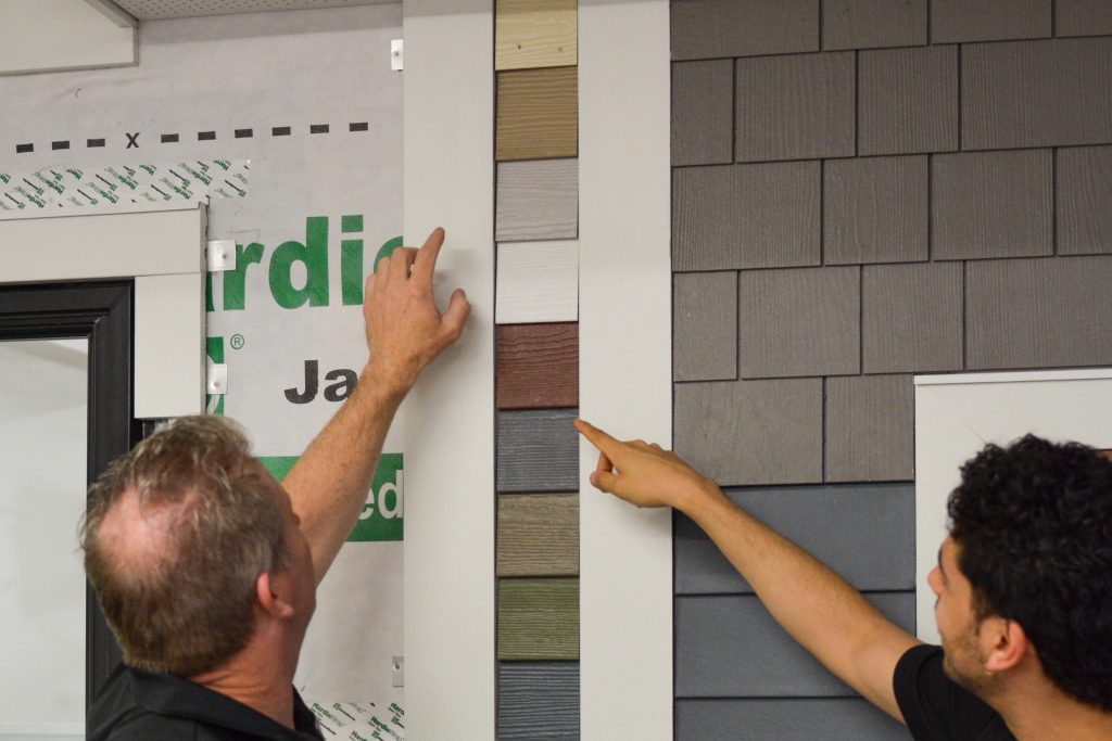 Two Patriot Contracting staff point out colors on a sample siding wall.